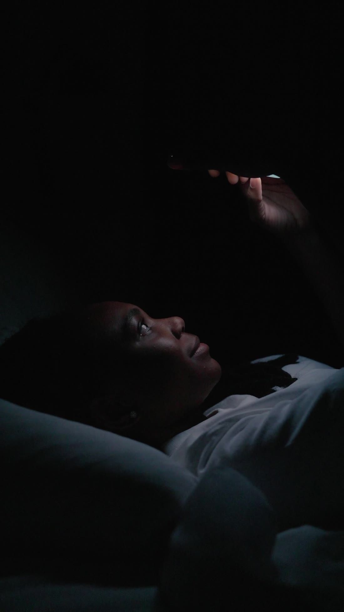 A person lying awake at night looking at a phone